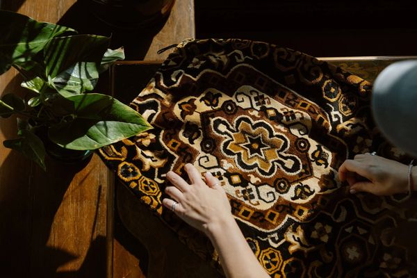Hands touching a patterned fabric beside a green plant on a wooden surface.
