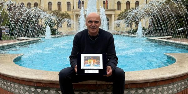 Man sitting by a fountain holding a framed picture with water jets spraying behind.