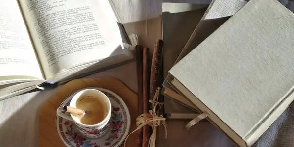 Books, cinnamon sticks, and a cup of coffee on a table.