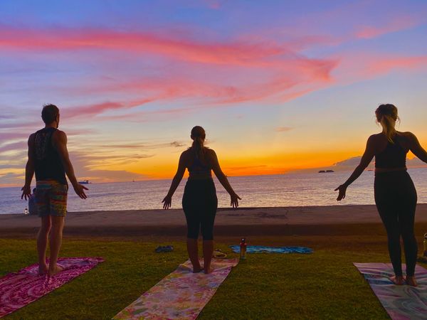 Three people doing mountain yoga pose in front of the beach in Hawaii under sunset sky