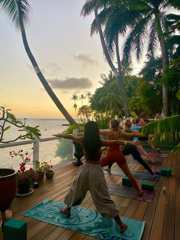 Group of people doing yoga at the beach house in warrior 2 pose facing the sunset in Honolulu, Oahu,