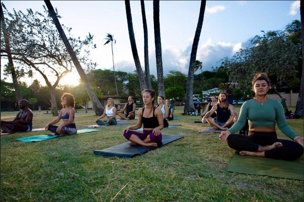 Group of yogis meditating oceanfront in the park in Honolulu for sunset yoga on the beach in Hawaii