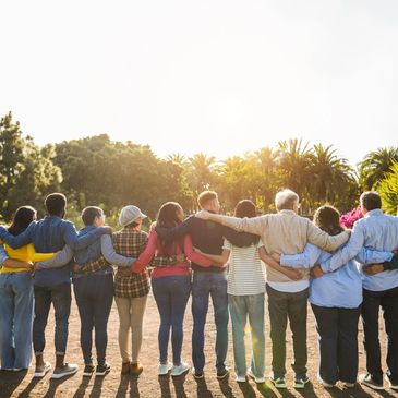 Group of diverse people standing arm in arm outdoors at sunset.