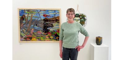 A smiling woman with glasses and short brown hair standing in front of colorful art on a white wall