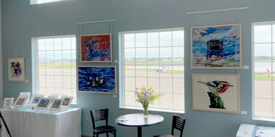Art show installed on light blue walls with large windows
