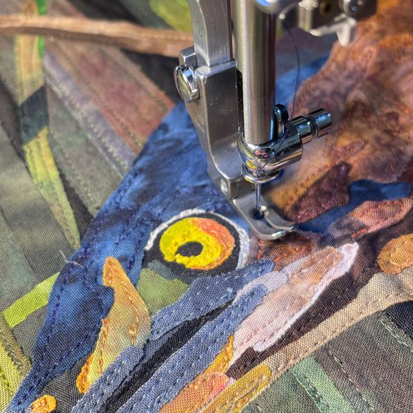 Close-up of sewing machine stitching a colorful bird design on fabric.