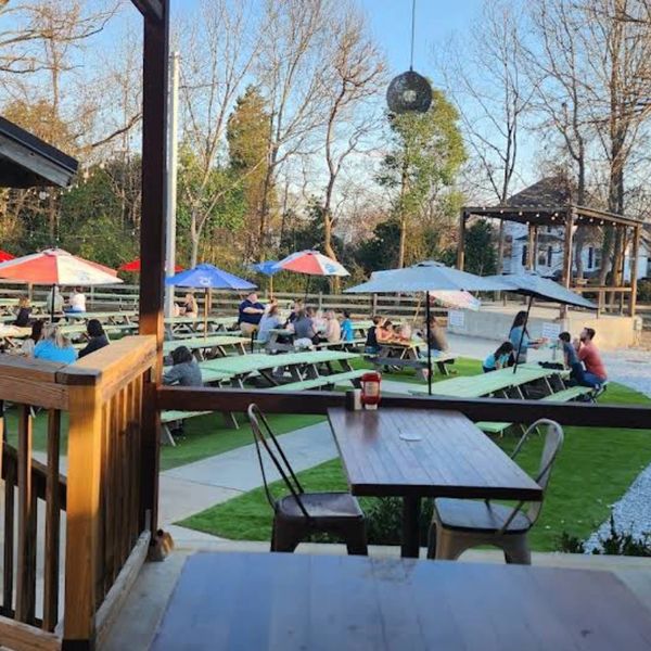 Outdoor seating area with picnic tables and umbrellas in a park-like setting.