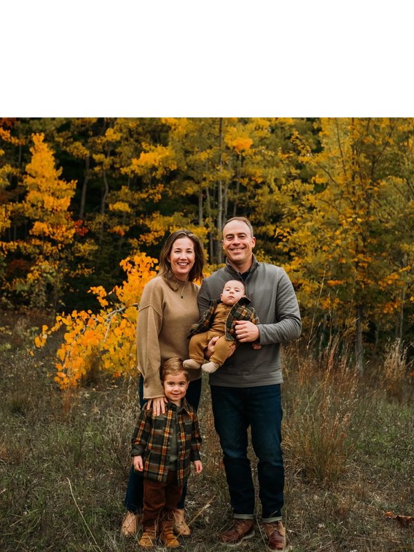 A family with two childrens standing in the forest posing for a picture.