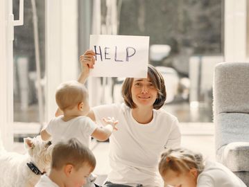 Woman holding a sign that says HELP surrounded by children indoors.