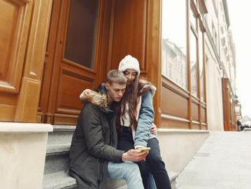 Young couple sitting on steps, looking at a smartphone together.