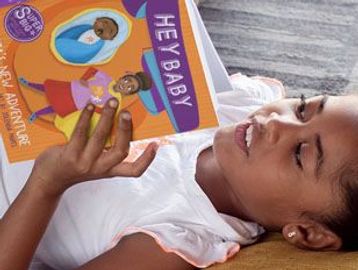 A child reading the colorful book 'Hey Baby' while lying down.