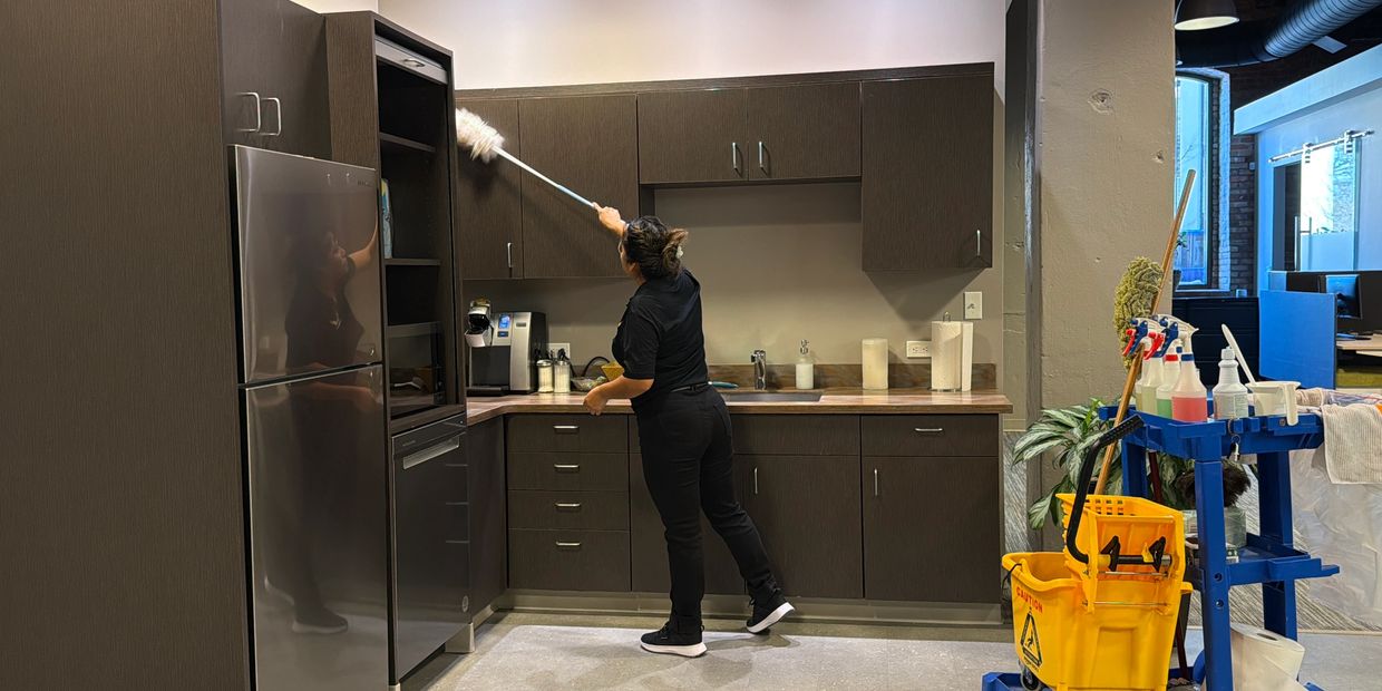 Aguilar Pro technician dusting kitchen cabinets in a office routine cleaning.