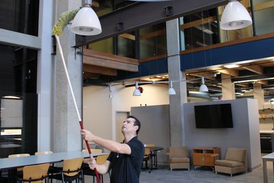 Aguilar Pro technician, dusting a chandelier in an office cleaning.