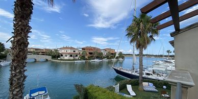 Boats docked in a peaceful marina with clear skies and palm trees.