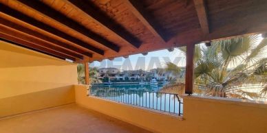 Spacious terrace with wooden roof overlooking a waterway and palm trees.
