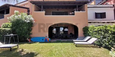 Modern townhouse with balcony, patio, and garden lounge chairs under bright sky.