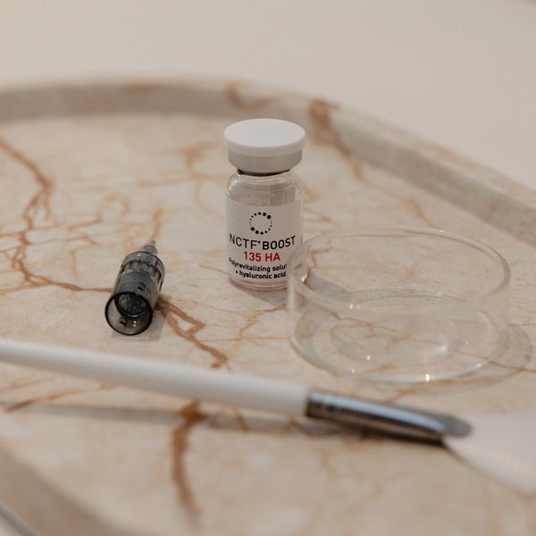 A vial of NCTF BOOST 135 HA with a syringe and brush on a marble tray.