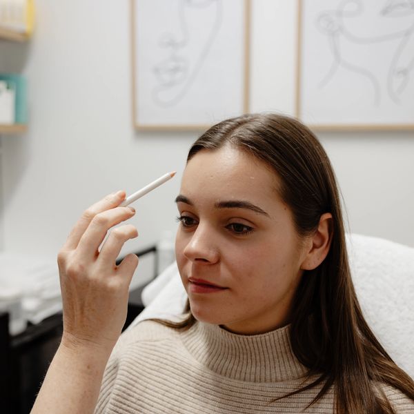 Woman holding a cosmetic pencil near her forehead in a beauty clinic.