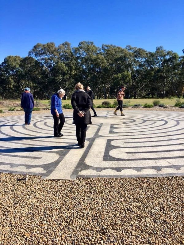 People walk thoughtfully through a large outdoor labyrinth on a sunny day.