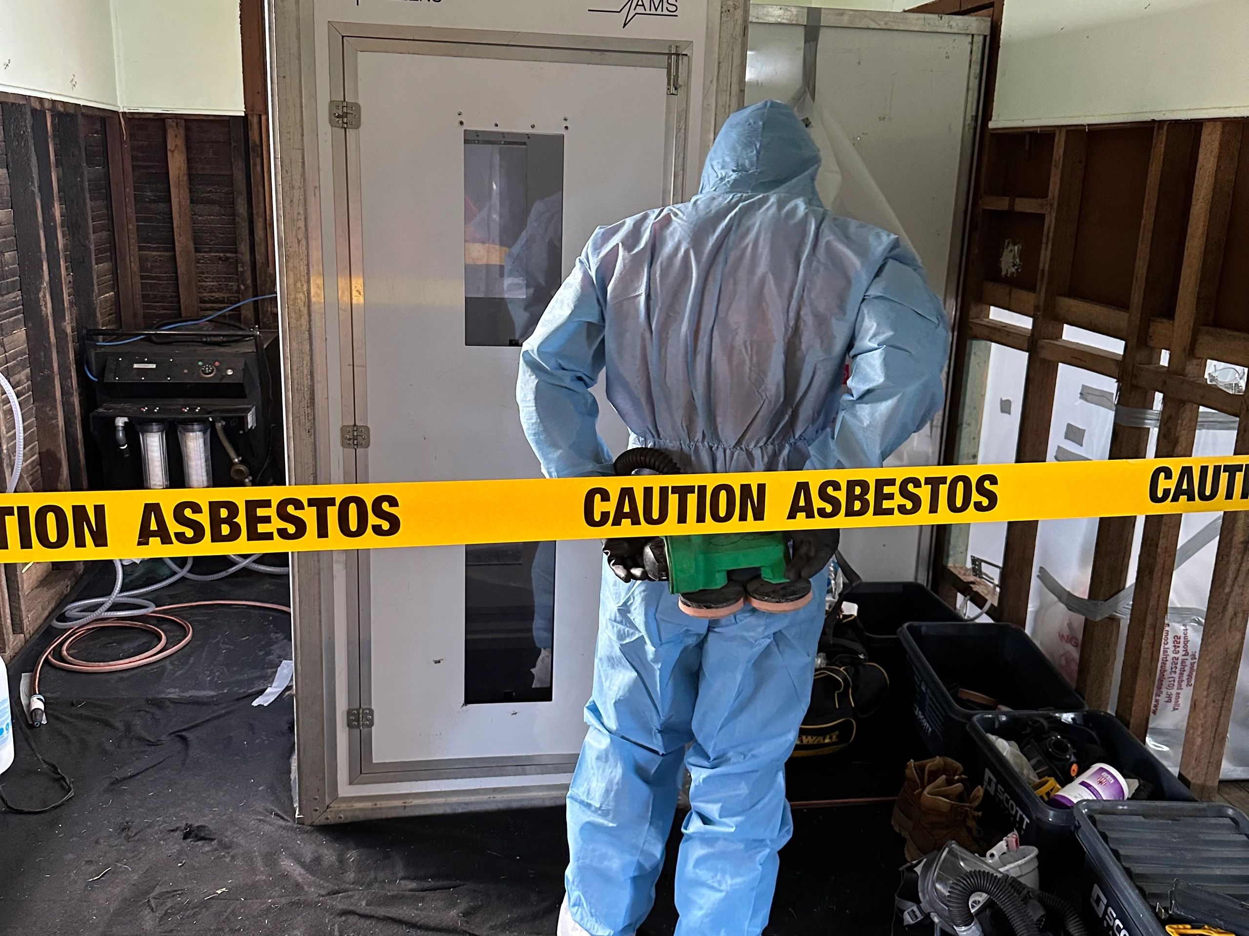 An asbestos removal technician suited up in hazmat PPE about to enter the asbestos removal work area
