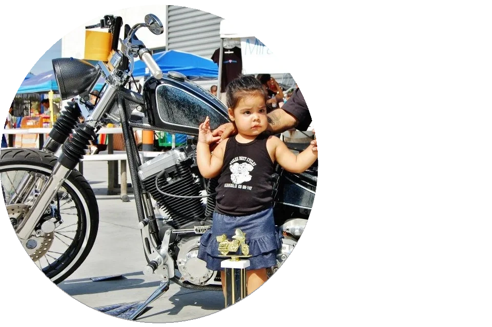 A toddler girl standing next to a motorcycle with a trophy in front.