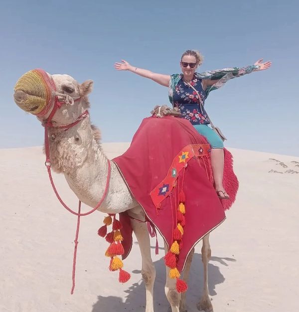 Woman joyfully riding a decorated camel in the desert.