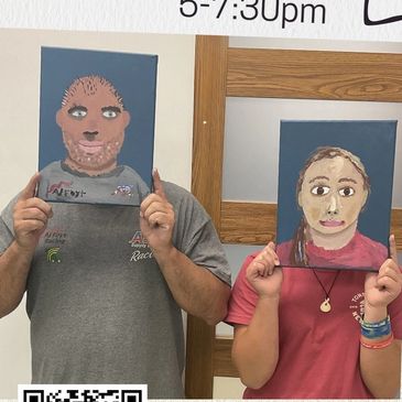 Two people holding hand-painted portraits in front of their faces.