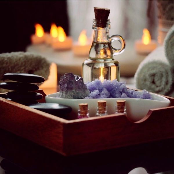 A serene spa setup with candles, essential oils, and crystals on a wooden tray.