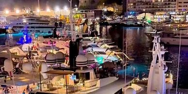 Luxury yachts docked at a vibrant marina at night.