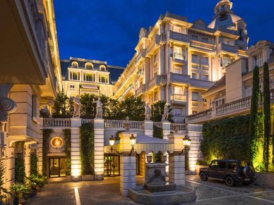 Elegant, illuminated hotel courtyard at dusk with classic architecture and vintage car.