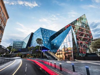 Modern angular glass building with dynamic reflections and city street.