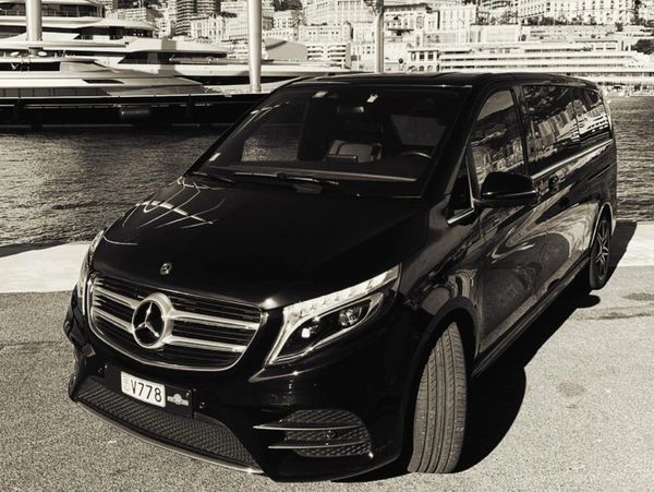 Black Mercedes luxury van parked near a waterfront with yachts.