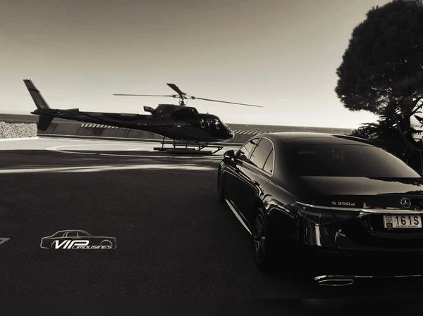 Luxury black Mercedes car beside a sleek helicopter on a private tarmac.