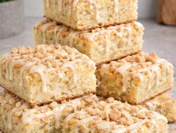 Stack of crumbly dessert bars with icing drizzle on top.