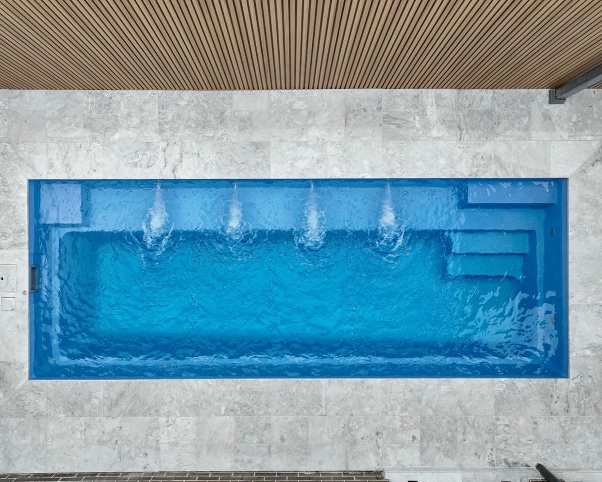 Top view of a small rectangular pool with water jets and stone tile surroundings.