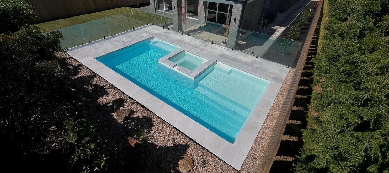 Modern backyard pool with an elevated spa and glass fencing.