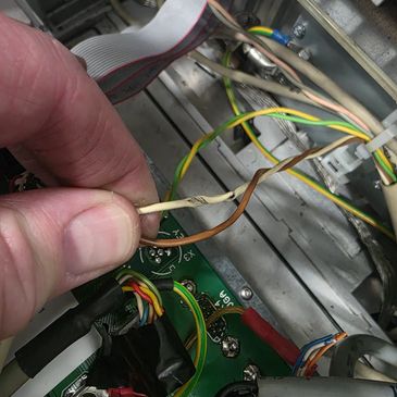 A hand holding a beige wire inside an electronic device with multiple colored wires.