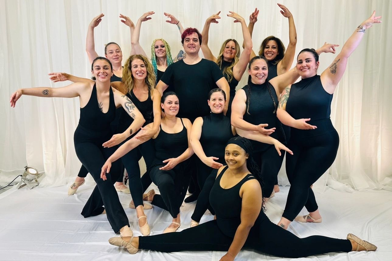 A diverse group of dancers in black outfits pose gracefully in a studio.