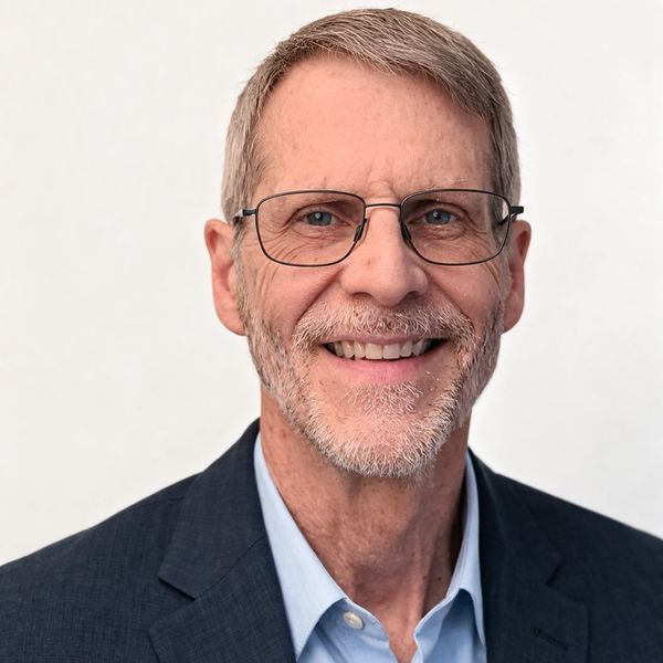Smiling middle-aged man with glasses in a suit jacket and blue shirt.