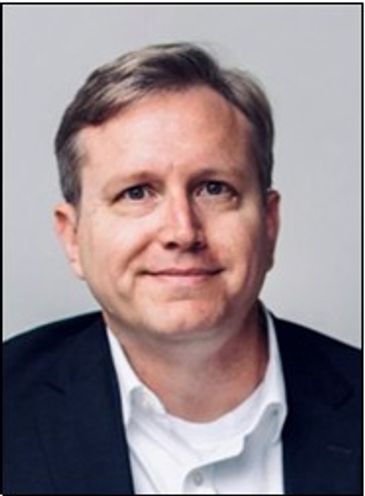 Man with light brown hair wearing a dark suit jacket and white shirt.