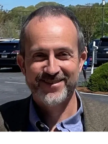 Smiling man outdoors with a beard and gray hair.