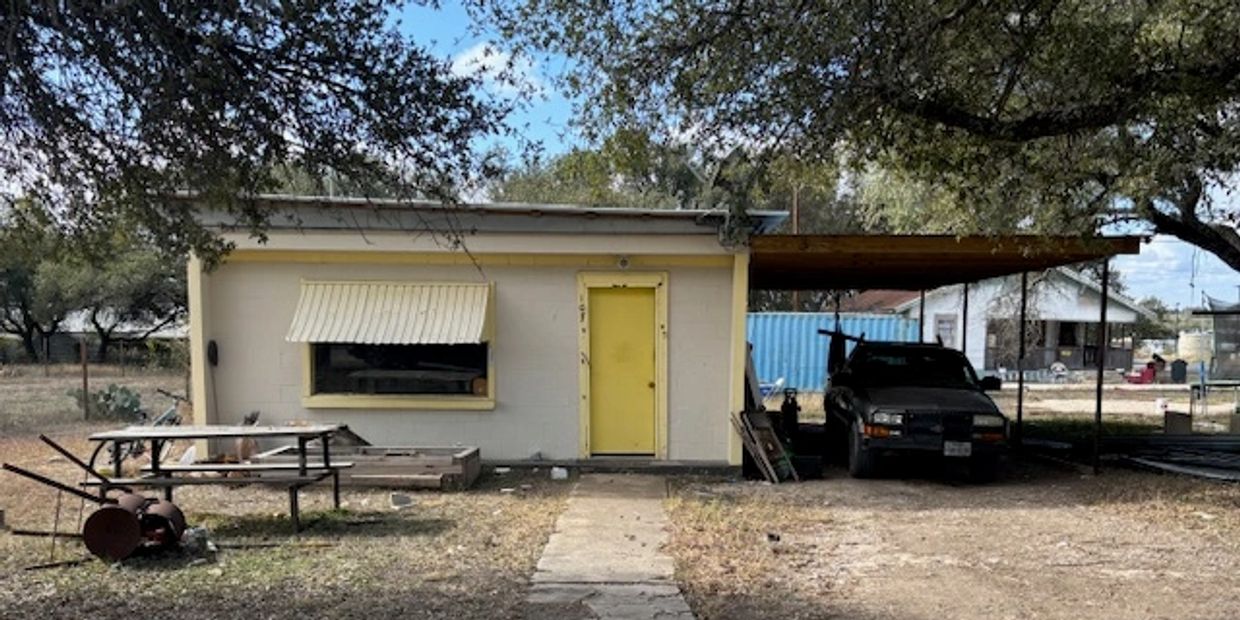 Small building with yellow door and covered carport.