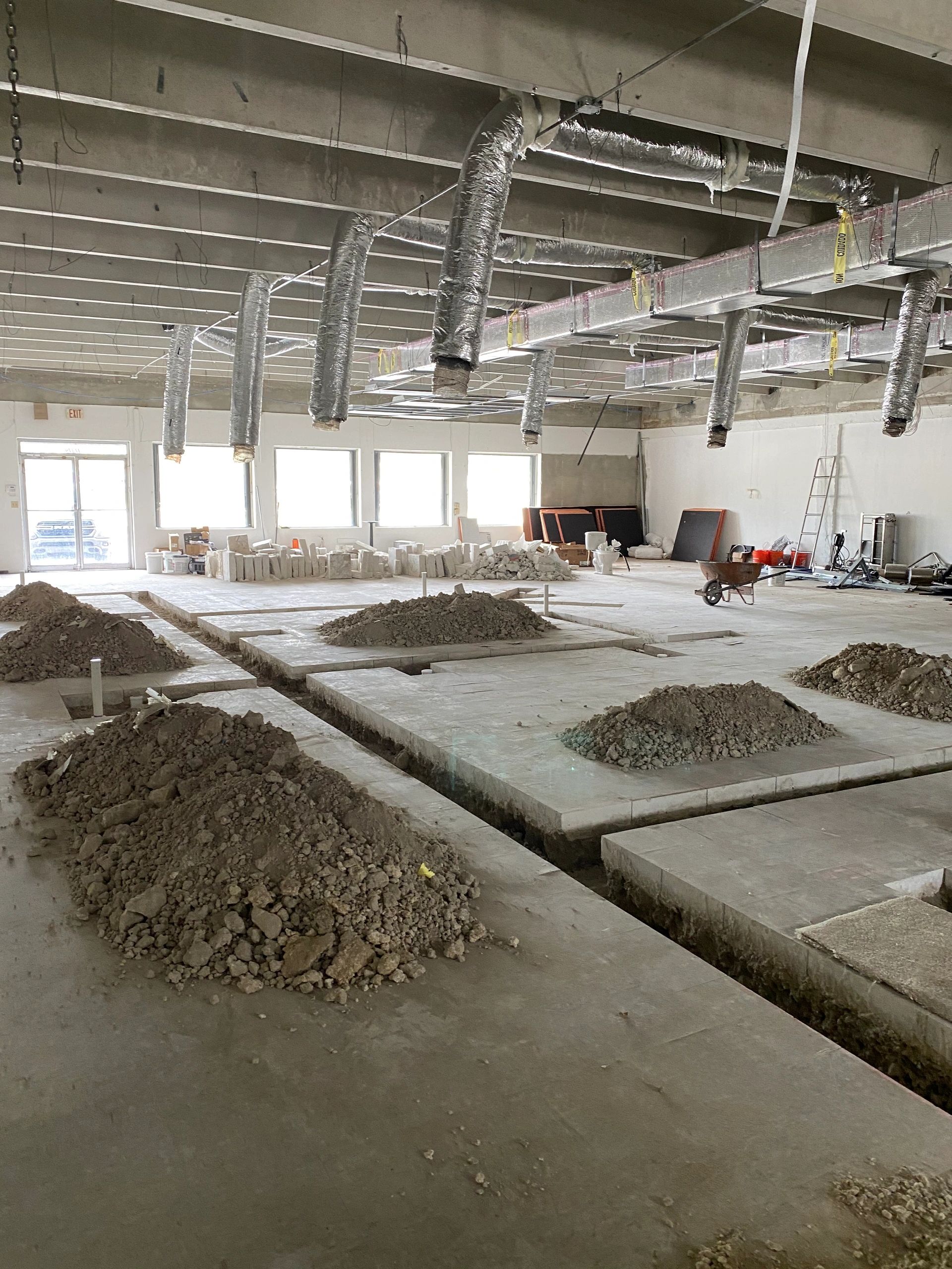 Interior of a building under construction with exposed HVAC ducts and dirt piles.
