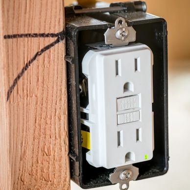 Close-up of a GFCI electrical outlet installed in a black box on a wooden stud.