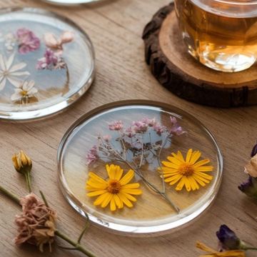 Clear resin coasters with embedded flowers on a wooden surface.