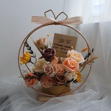 Elegant floral arrangement in a circular frame with soft pastel roses and a ribbon bow.