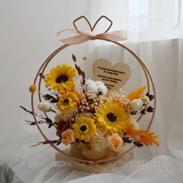 A charming floral arrangement with sunflowers in a circular frame and a heart-shaped note.