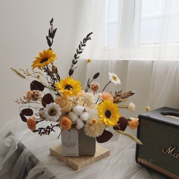 A charming flower arrangement with sunflowers and soft pastel blooms in a cozy indoor setting.