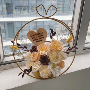 Elegant floral arrangement in a circular frame with pastel roses and a heart-shaped note.