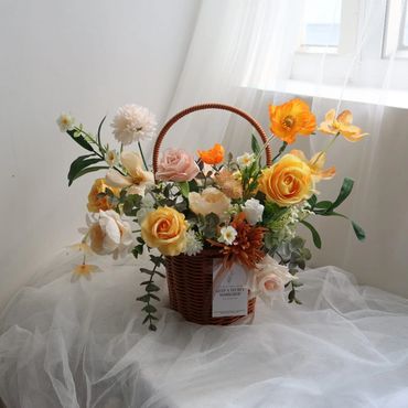 A basket filled with colorful artificial flowers on a white fabric near a window.